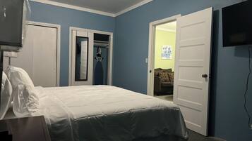 Un dormitorio con cama, televisor, armario y puerta que da a otra habitación.