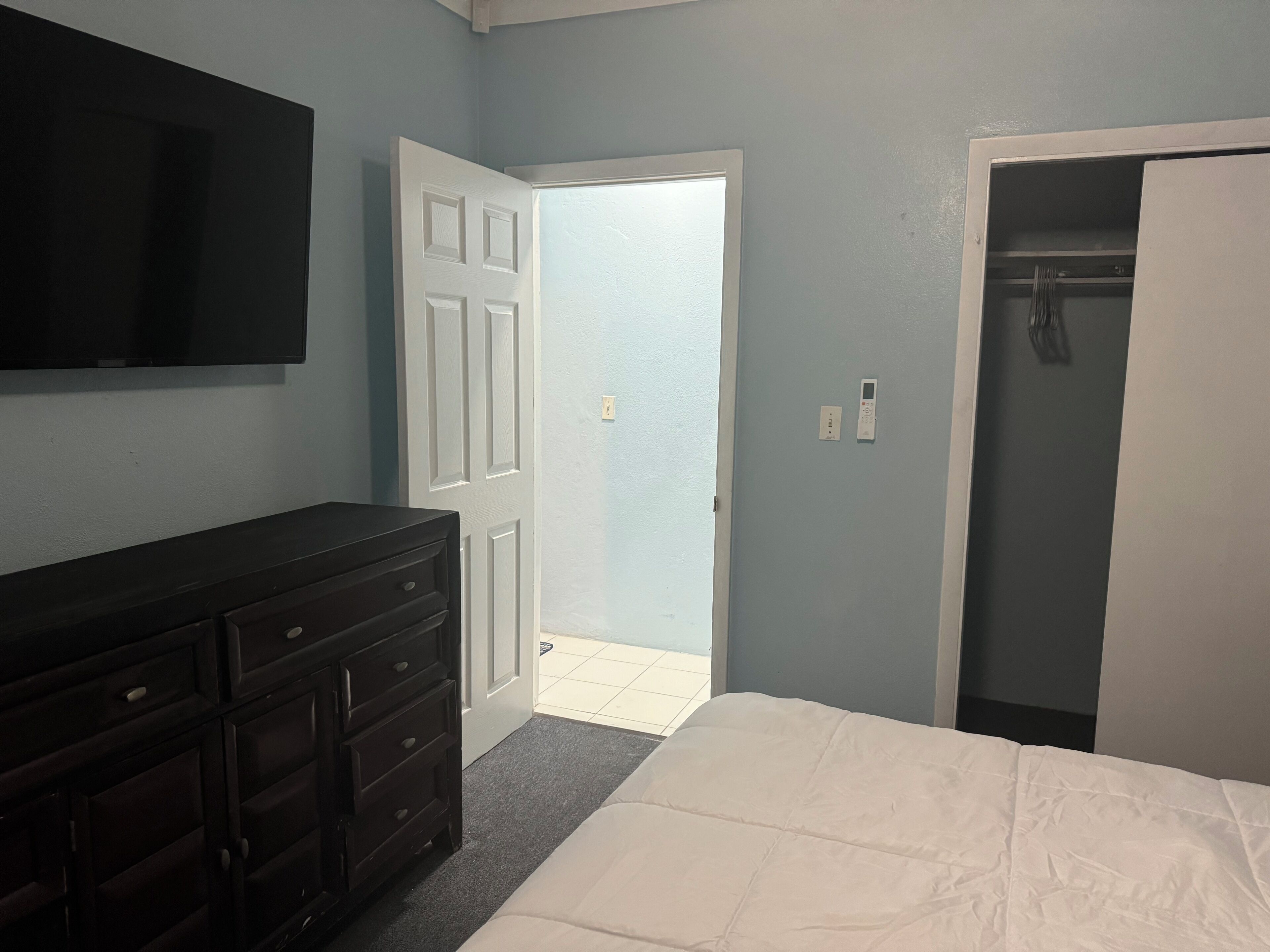 A bedroom with a bed, dresser, TV, and closet.