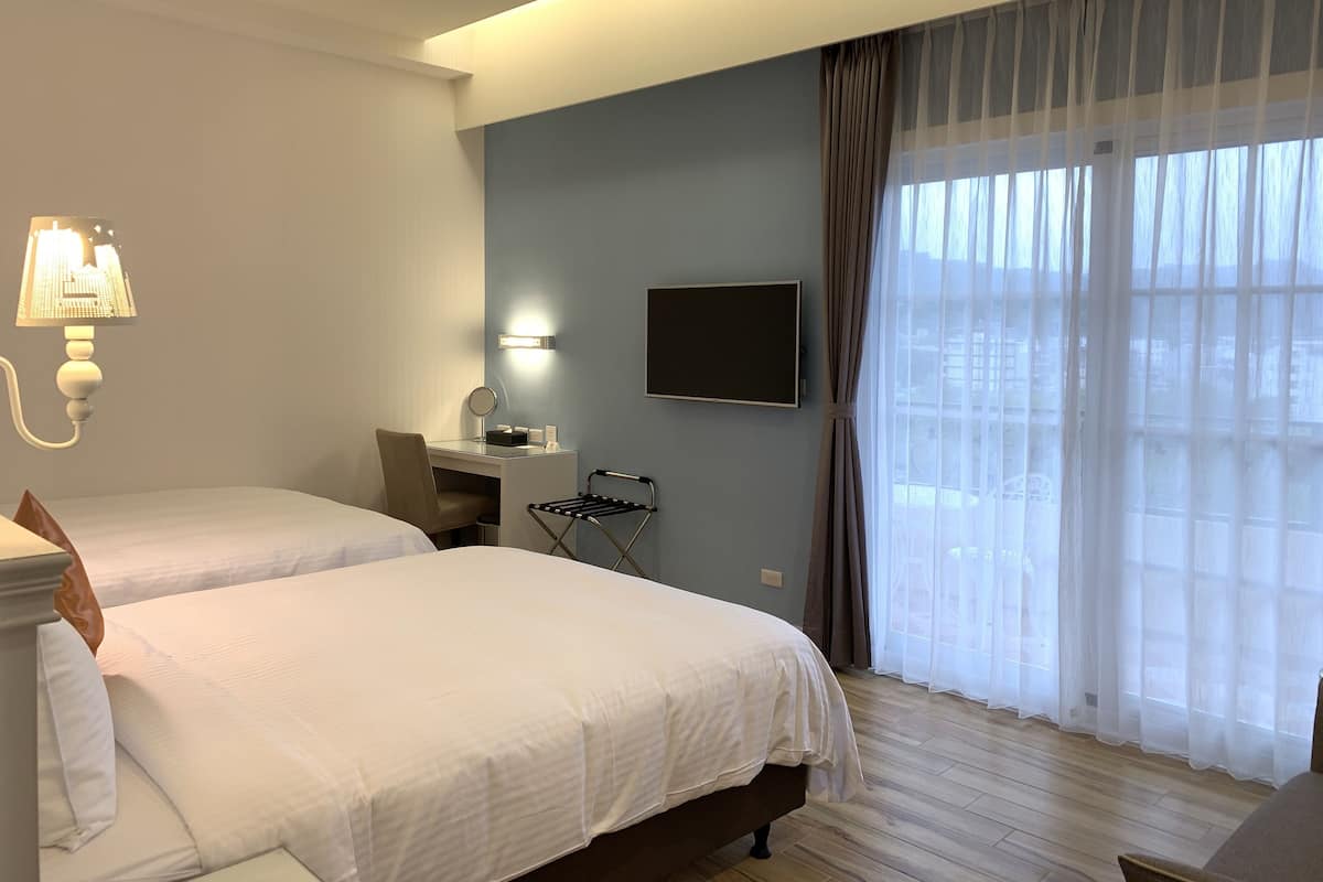 A hotel room with two beds, a desk with a chair, a TV, and a window with curtains.