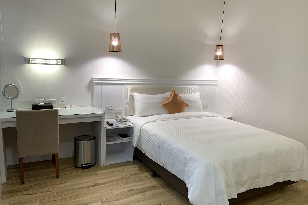 A neatly arranged bedroom with a bed, bedside table, and a desk with a chair.