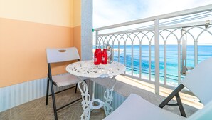Un pequeño balcón con una mesa y sillas blancas, dos botellas de vino rosado y vistas al mar.