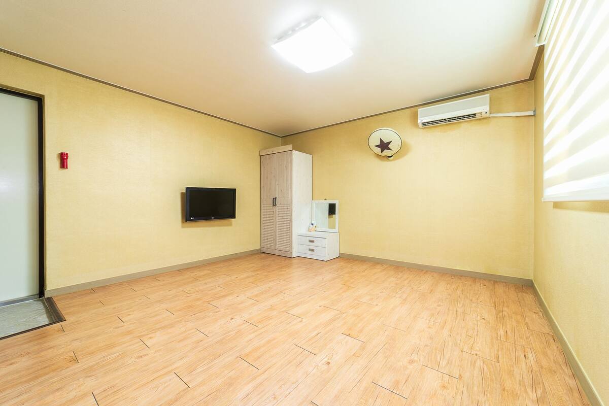A room with a wooden floor, a flat-screen TV mounted on the wall, a wardrobe, and a ceiling fan.