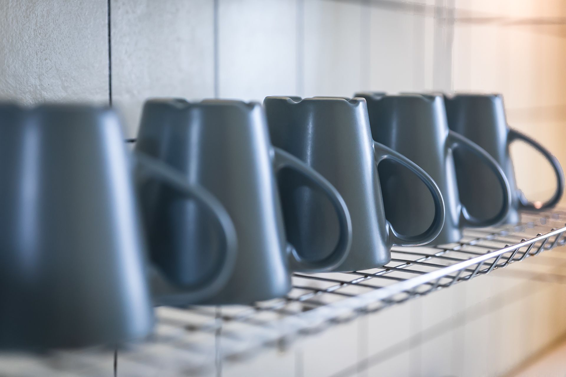 A row of grey mugs on a metal rack.