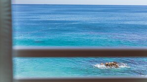 Vista del océano a través de una ventana, con una formación rocosa visible en el agua.