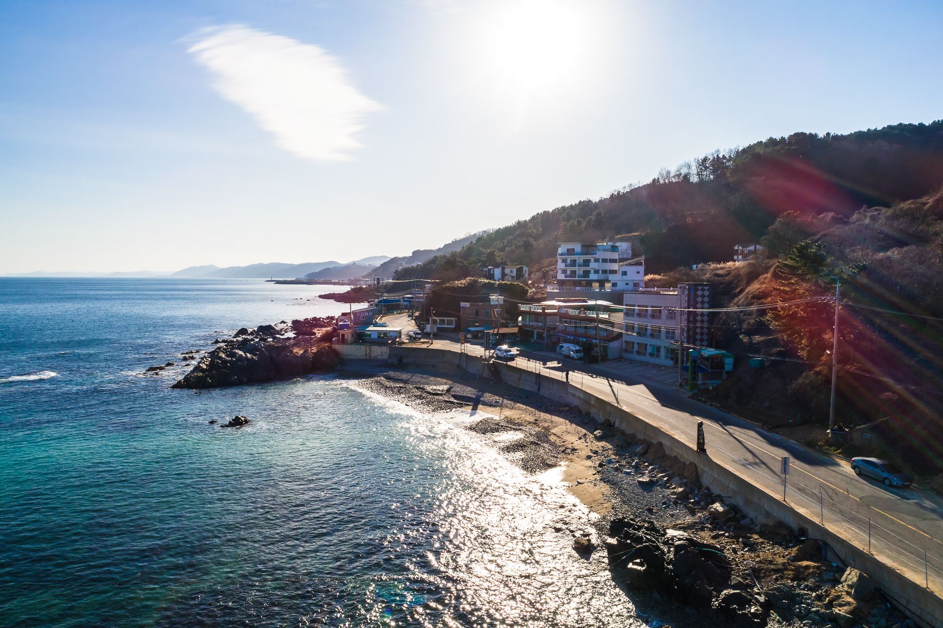 A coastal road with buildings on the hillside, overlooking the sea.