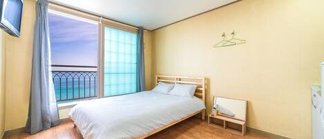 Un dormitorio con cama, una mesita de noche, cortinas en la ventana y vista al océano.
