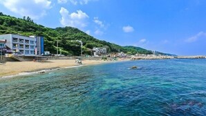 Una playa con aguas cristalinas, una orilla de arena y edificios al fondo.