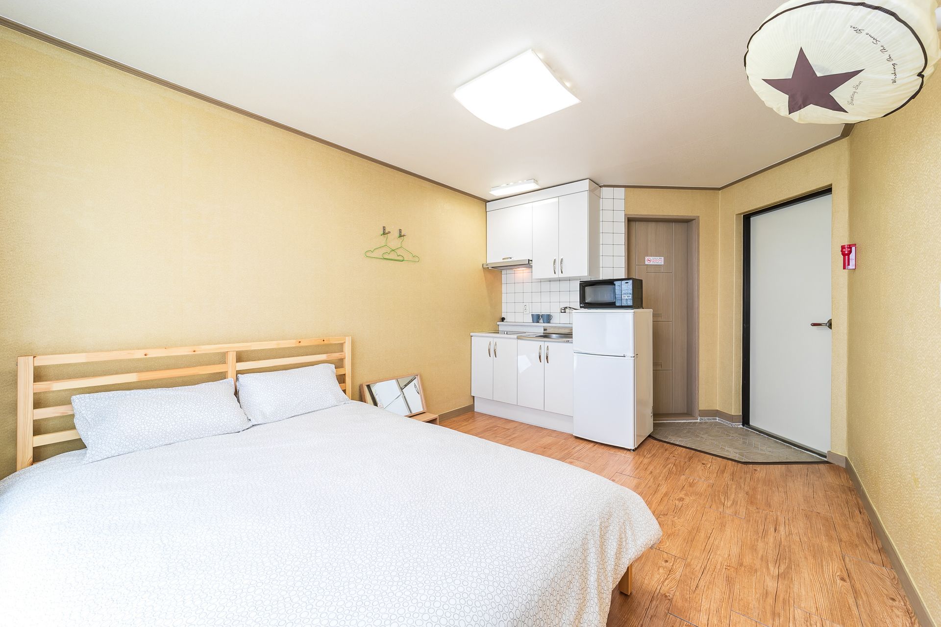 A compact bedroom with a bed, a kitchenette, and a door.