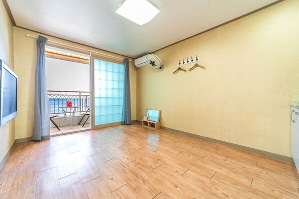 A spacious room with a wooden floor, a large sliding glass door leading to a balcony with a view of the sea, a small table with a chair, and a wall-mounted clock. - Haelim Pension (Yeongdeok)