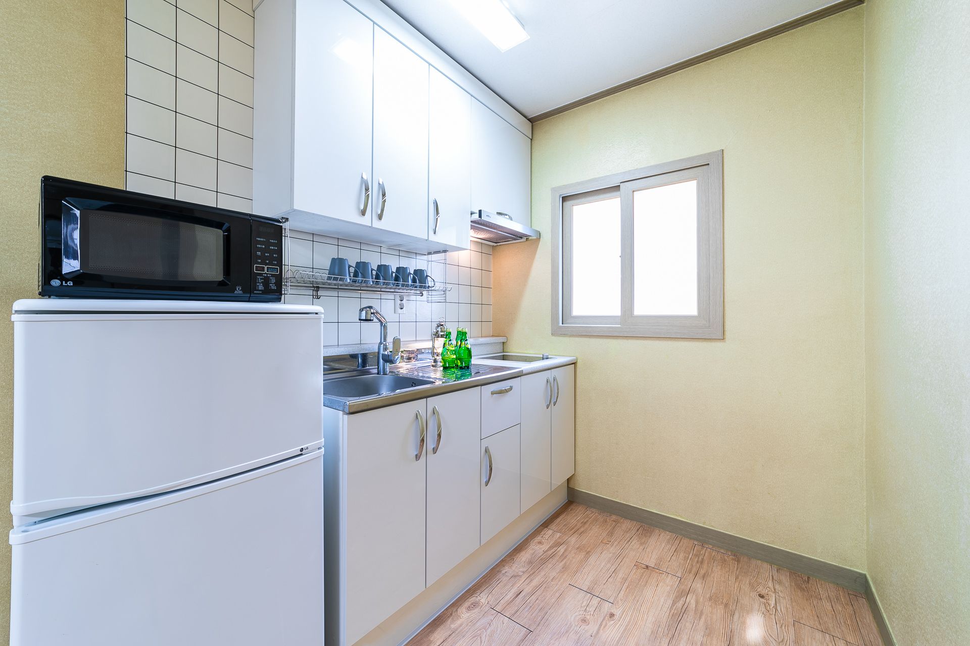 A compact kitchen with white cabinets, a microwave, a sink, and a window.