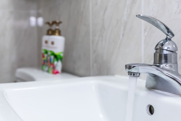 Un lavamanos con agua corriente, un dispensador de jabón y una pared de mármol al fondo.