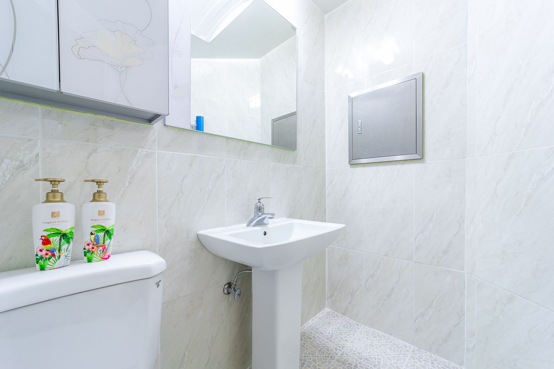 A bathroom with a white sink, a toilet, and two bottles of Tropicel Holiday body wash.