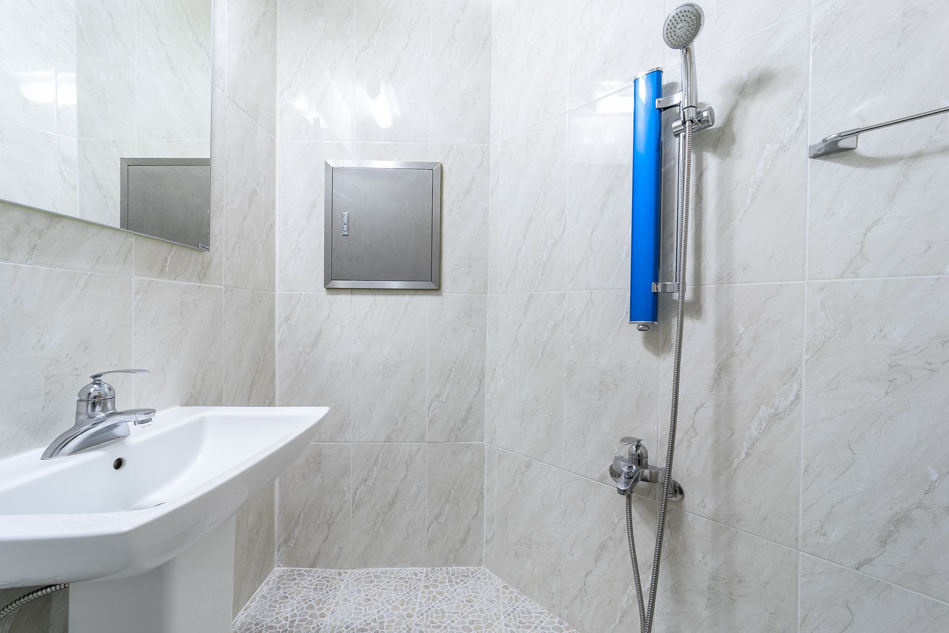 A bathroom with a white sink, a handheld showerhead, and a wall-mounted control panel.