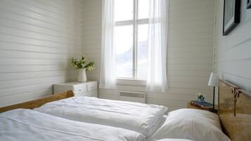 Une chambre avec deux lits, une table de chevet avec une lampe, une fenêtre avec des rideaux et une vue sur les montagnes.