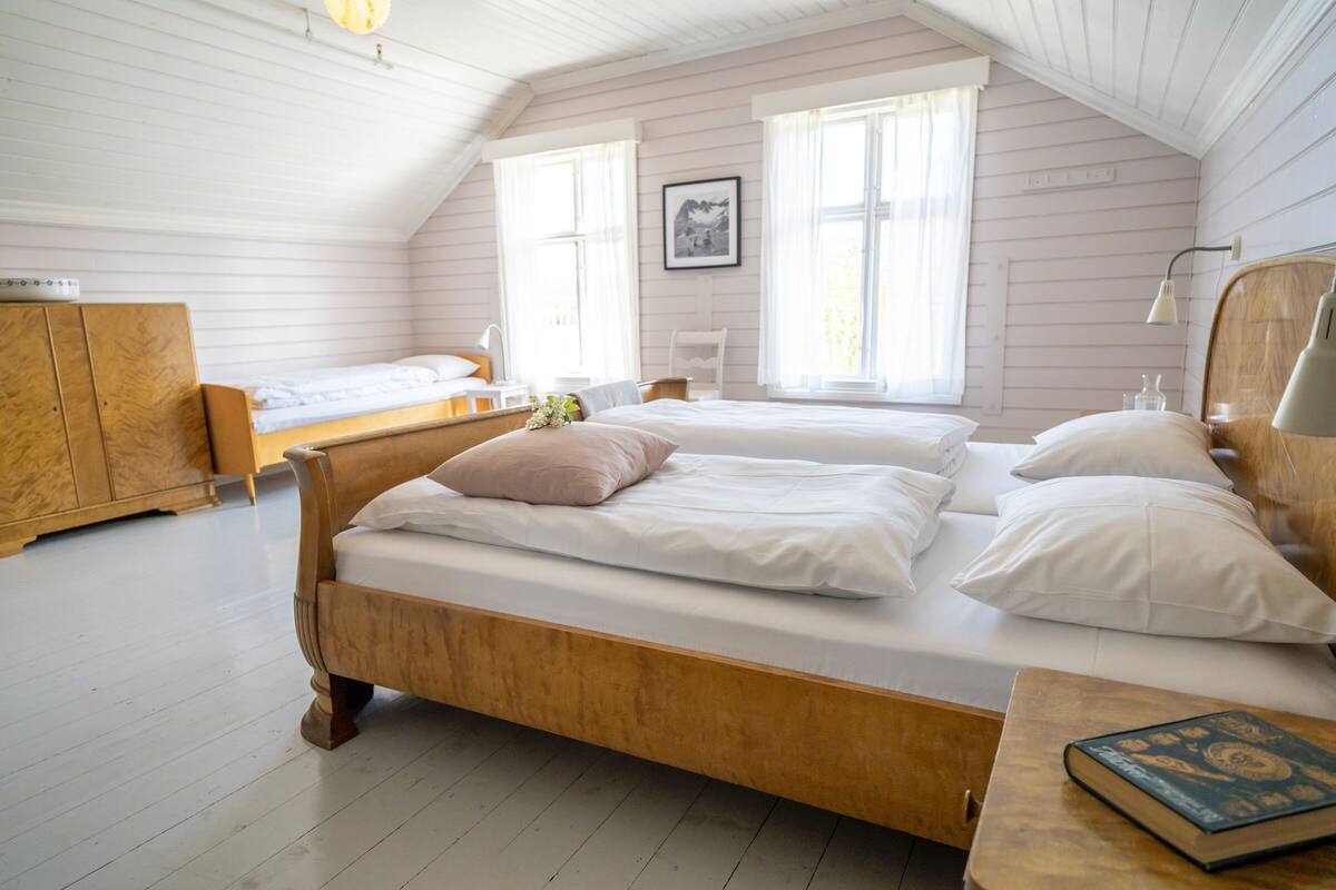 A cozy, well-lit room with a wooden bed, a small desk, and a window with curtains.