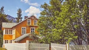 A wooden house with a balcony, surrounded by a white picket fence and lush greenery. - Sommerhotellet (Vang)