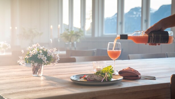 A table with a glass of orange juice, a plate with food, a vase with flowers, and a candle. - Sommerhotellet (Vang)
