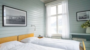 A bedroom with two beds, a window with white curtains, and two framed pictures on the wall. - Sommerhotellet (Vang)
