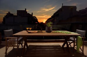 Una terrassa al terrat amb una taula de fusta preparada per a dues persones, una planta en test i una vista al capvespre.