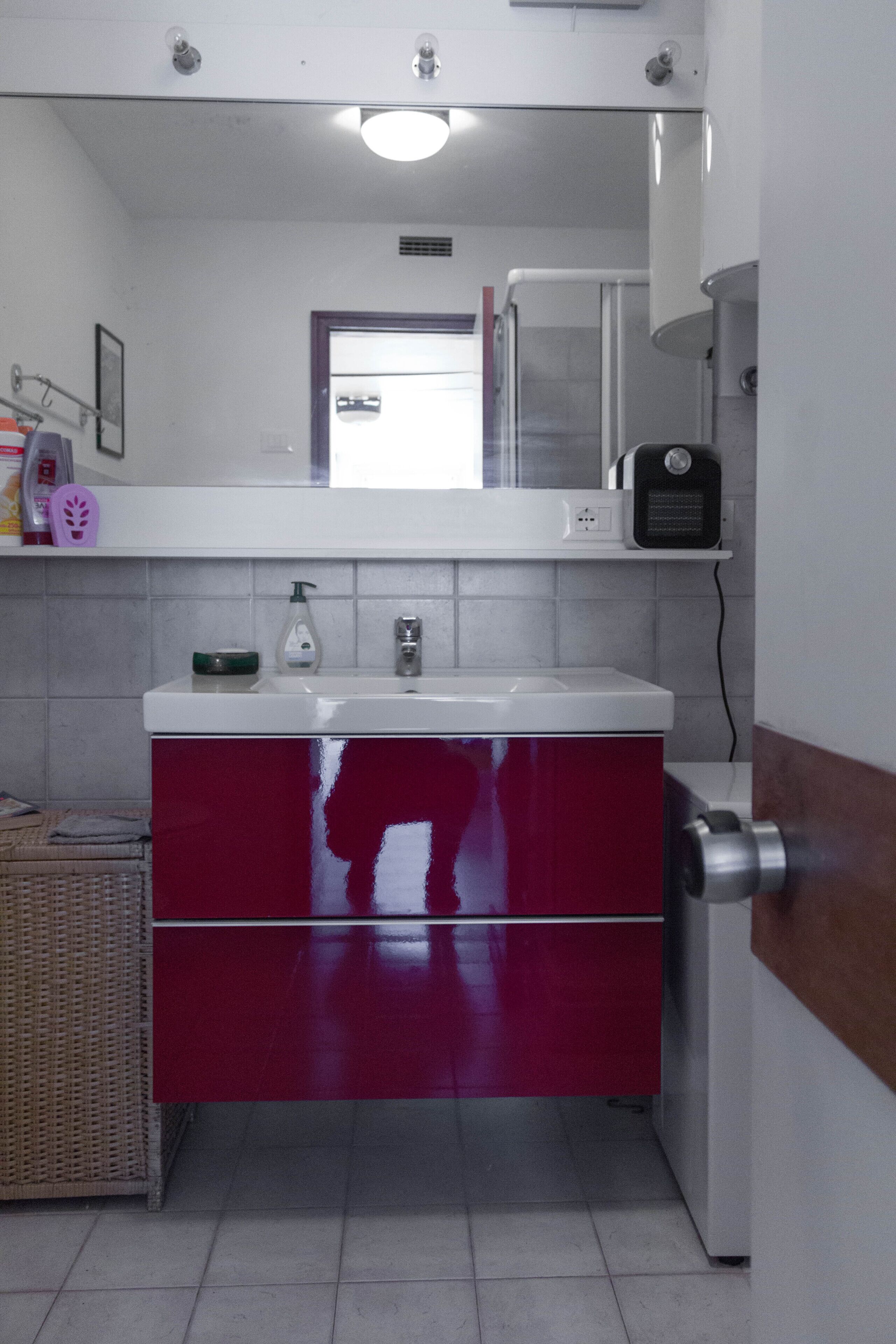 A bathroom with a white sink, red cabinet, and a mirror above it.