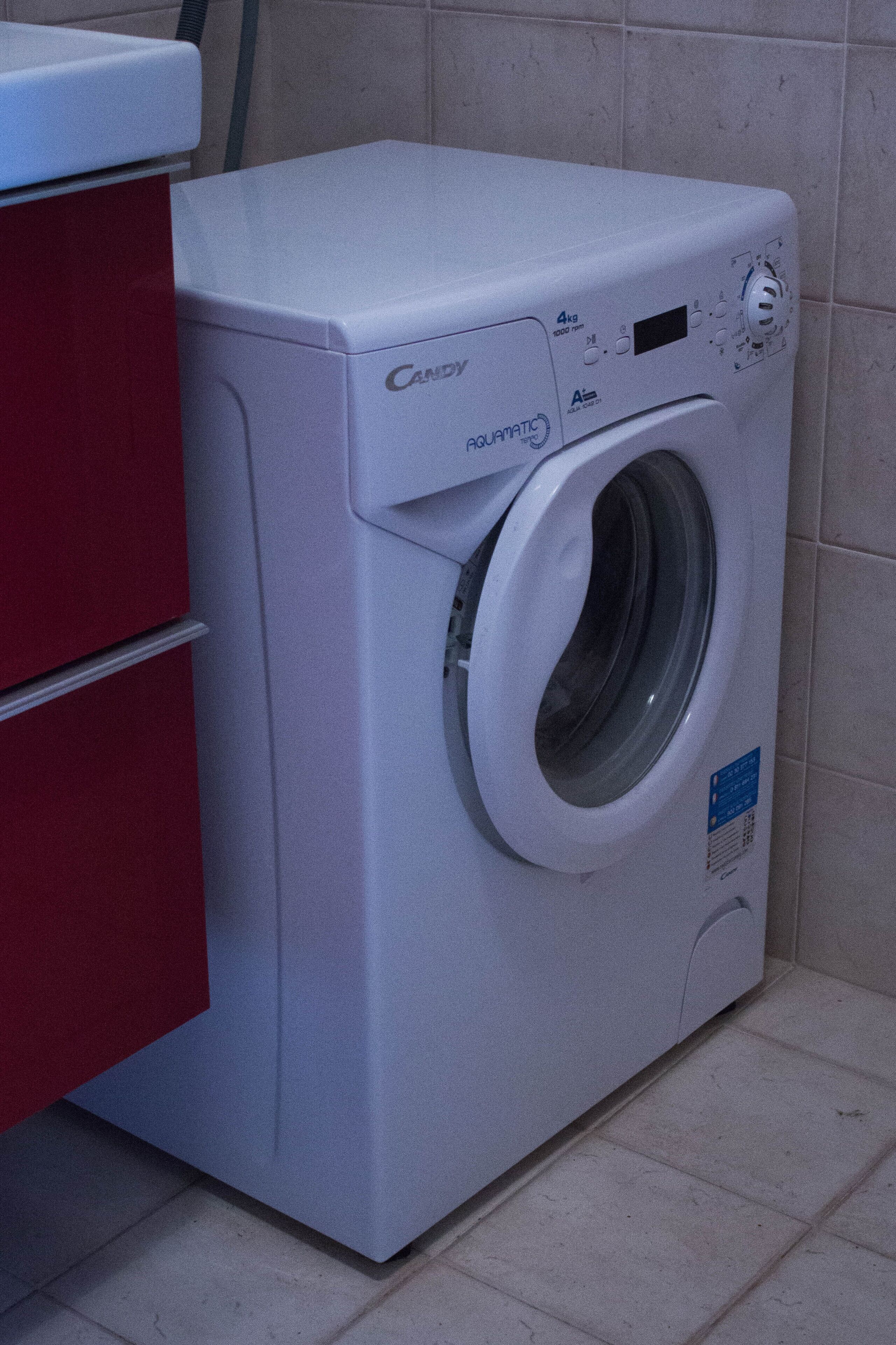 A white Candy Aquatic front-loading washing machine in a bathroom with beige tiles.