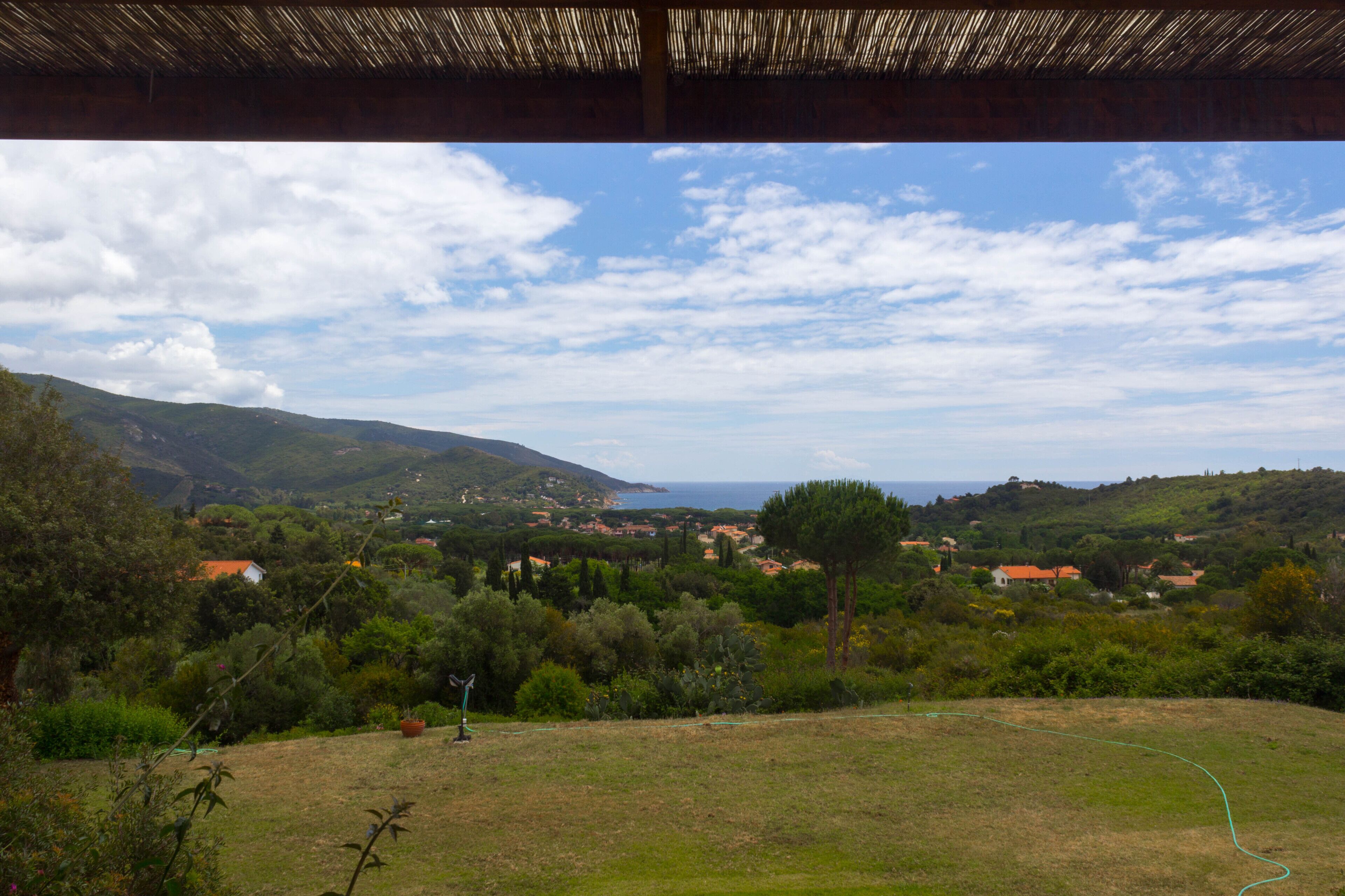 A view from a covered area overlooking a coastal landscape with hills, trees, and a few buildings.