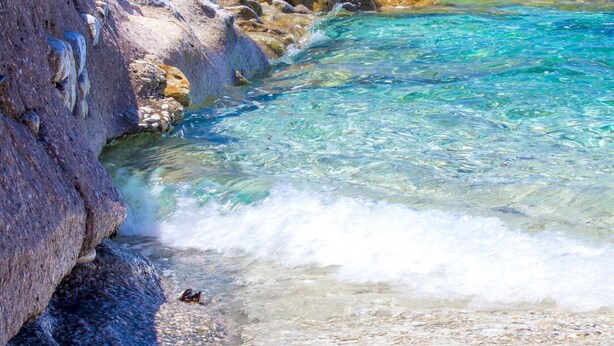 Un paisaje costero con aguas turquesas cristalinas, acantilados rocosos y una playa arenosa.