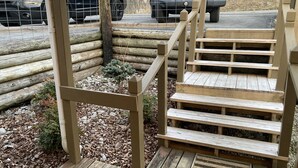 A wooden staircase leading up to a log cabin, surrounded by a gravel path and a small tree.