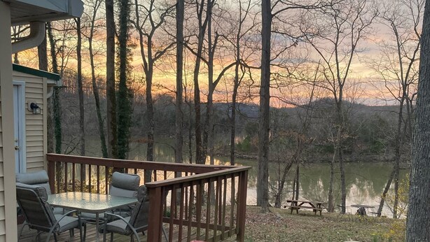 A deck with outdoor furniture, a covered grill, and a view of a lake surrounded by trees.