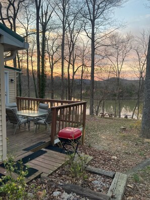 A deck with outdoor furniture, a covered grill, and a view of a lake surrounded by trees.