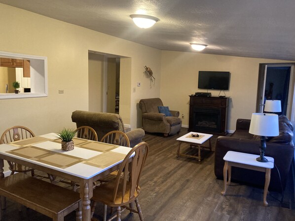 A living room with a dining table, chairs, a sofa, a TV, and a fireplace.