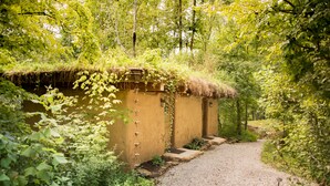 A rustic building with a thatched roof, surrounded by dense greenery and a gravel path leading to it. - Makanda Inn (Makanda)