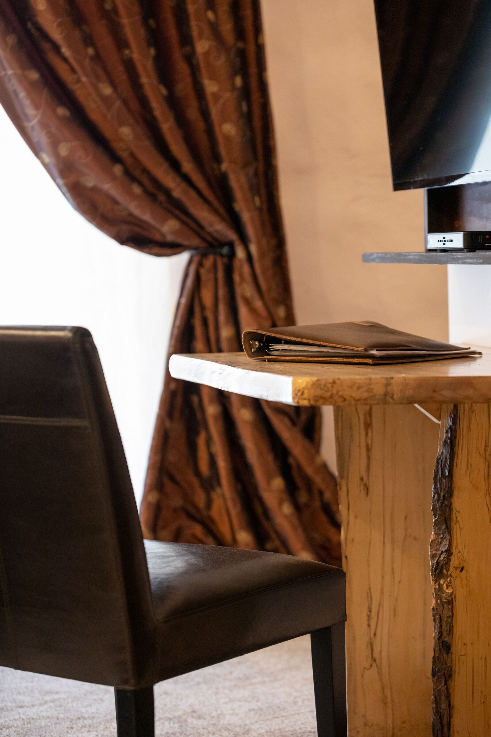 Une table en bois, une chaise en cuir, un carnet en cuir fermé et un téléviseur posé sur un meuble.