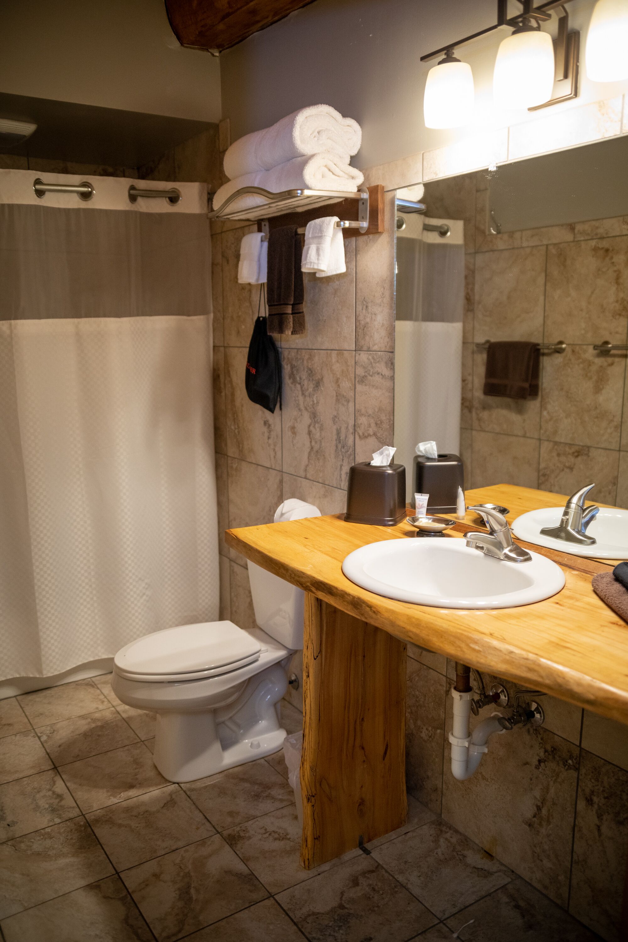 A bathroom with a wooden vanity, two sinks, a toilet, and a shower.