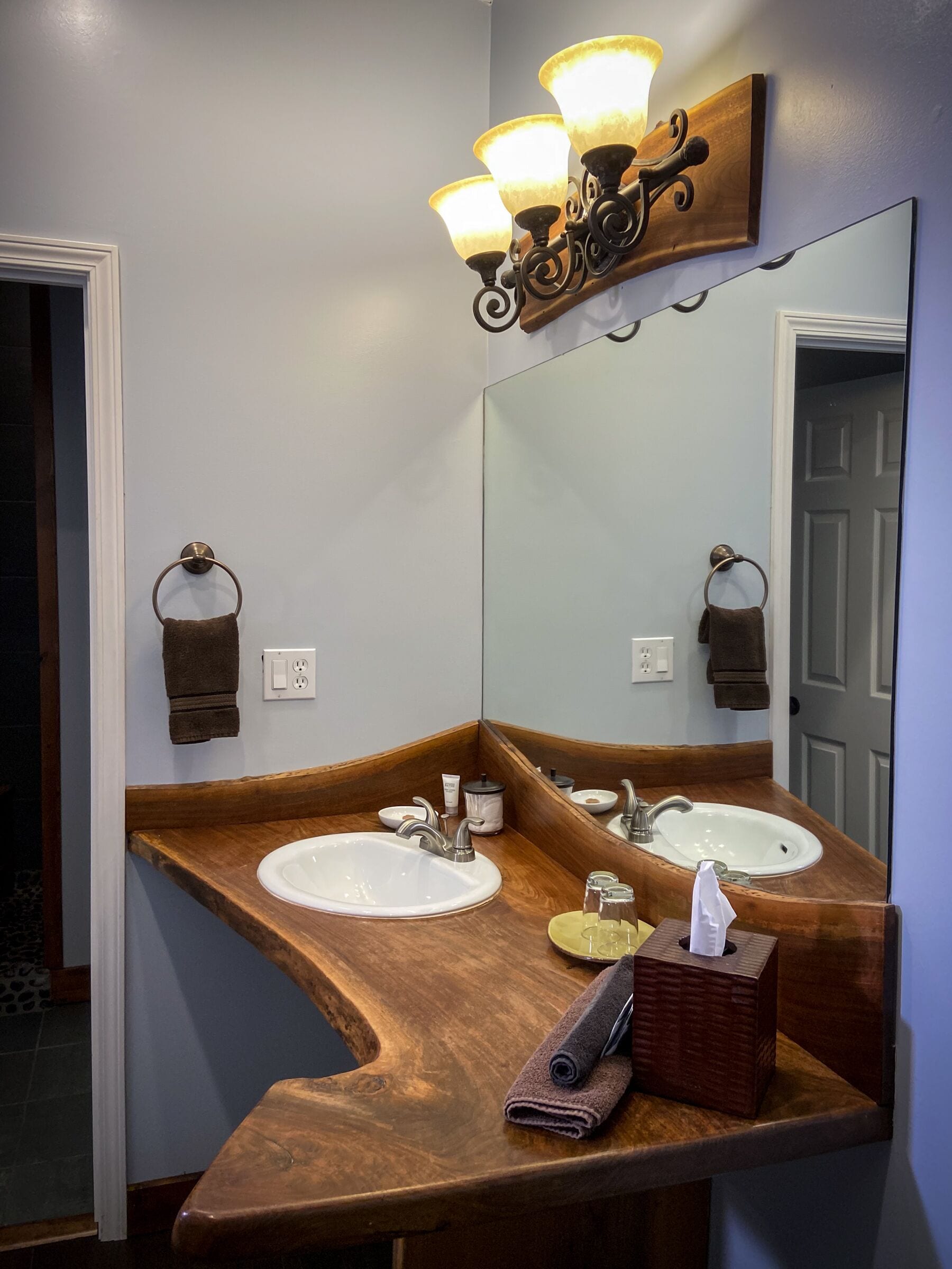 A bathroom with two sinks, a wooden vanity, a mirror, and a wall-mounted light fixture.