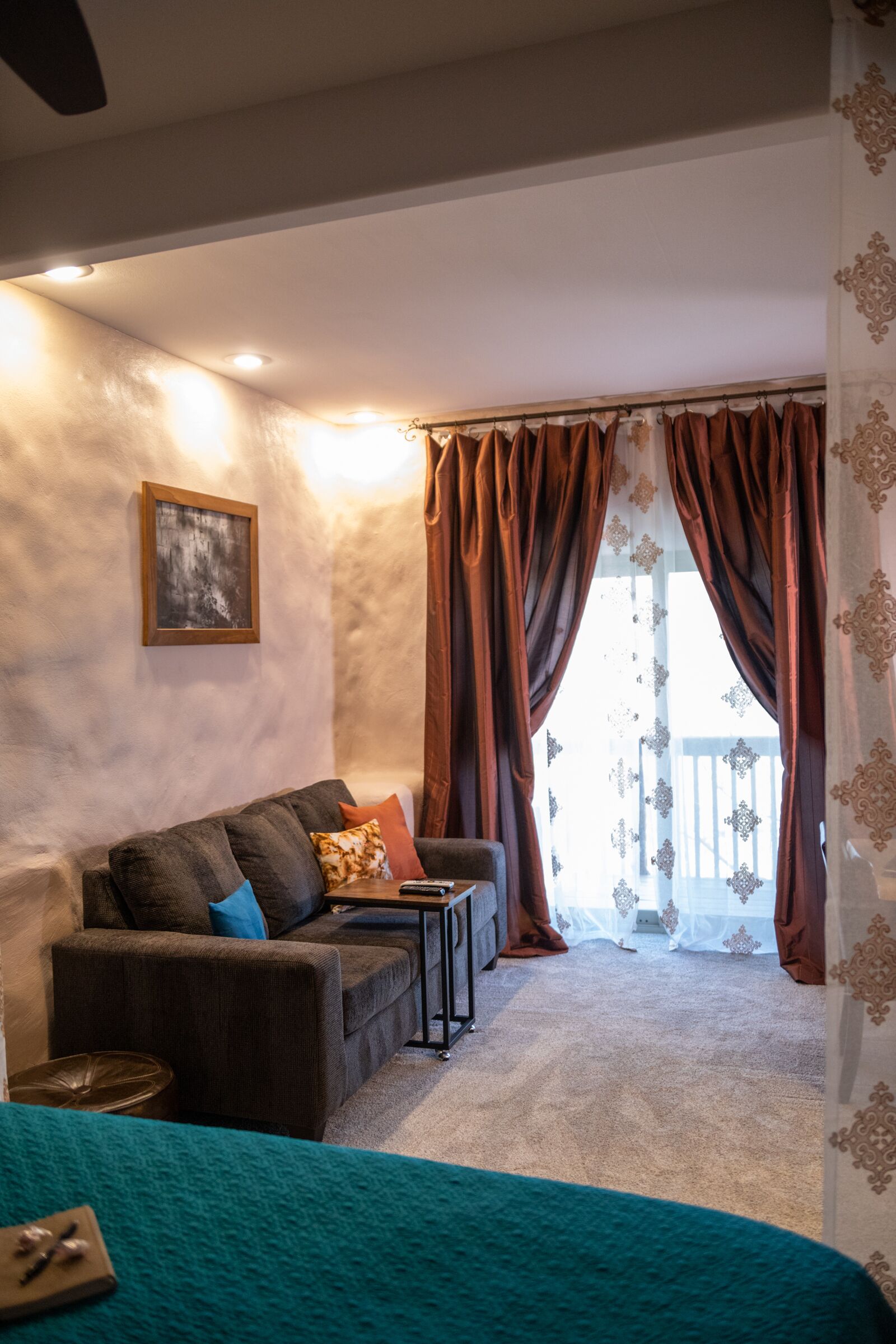 Un salon chaleureux avec un canapé, une petite table et une vue sur un balcon extérieur, visible à travers de grandes rideaux.