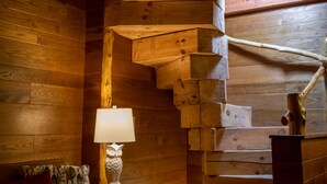 A cozy log cabin interior with a wooden staircase, a cushioned sofa, a small table, and a lamp. - Makanda Inn (Makanda)