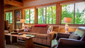 A cozy living room with a brown leather sofa, a wooden coffee table, and a window with a view of trees. - Makanda Inn (Makanda)