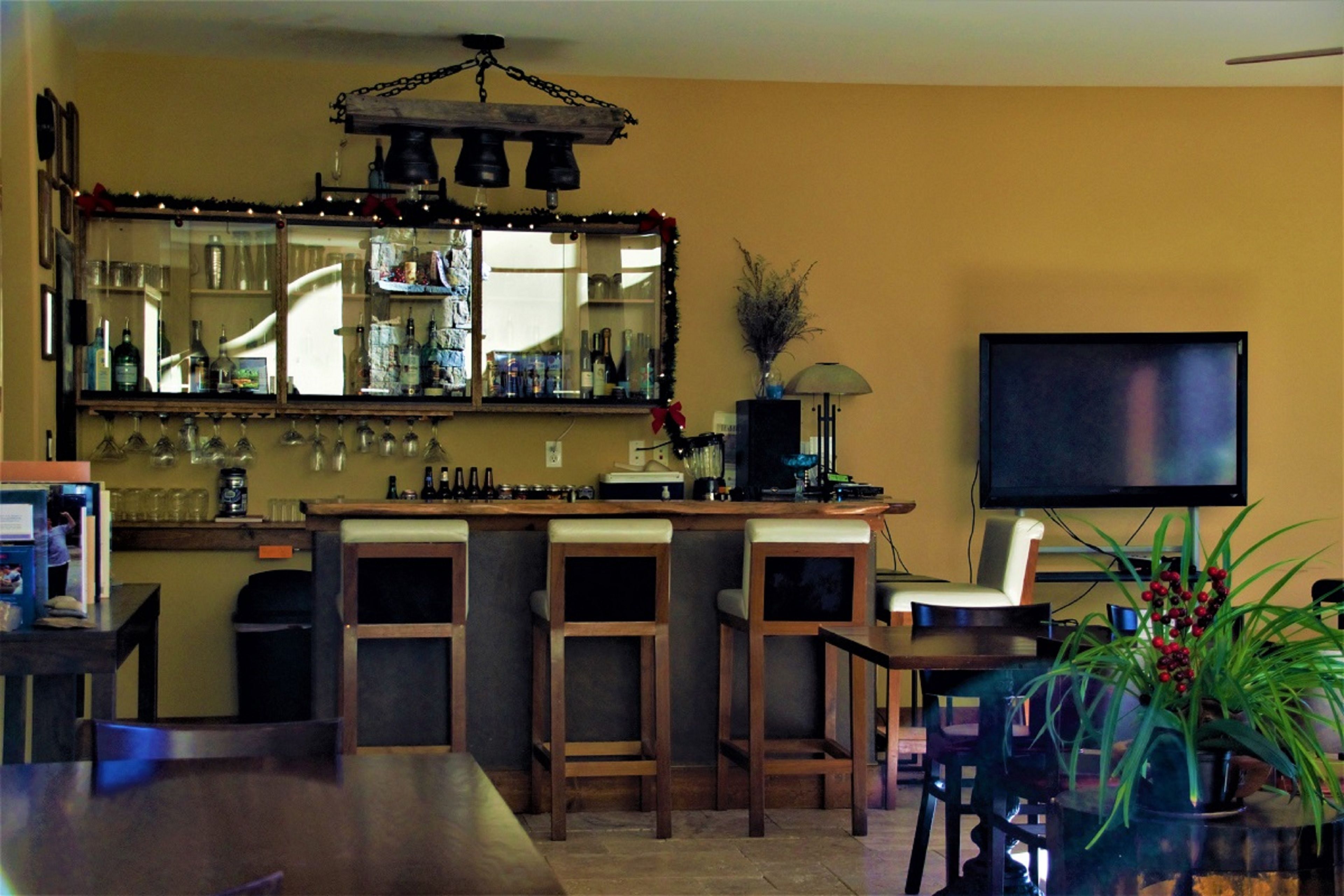 Zona de bar con un espejo, estanterías llenas de botellas, un televisor y una planta en maceta.