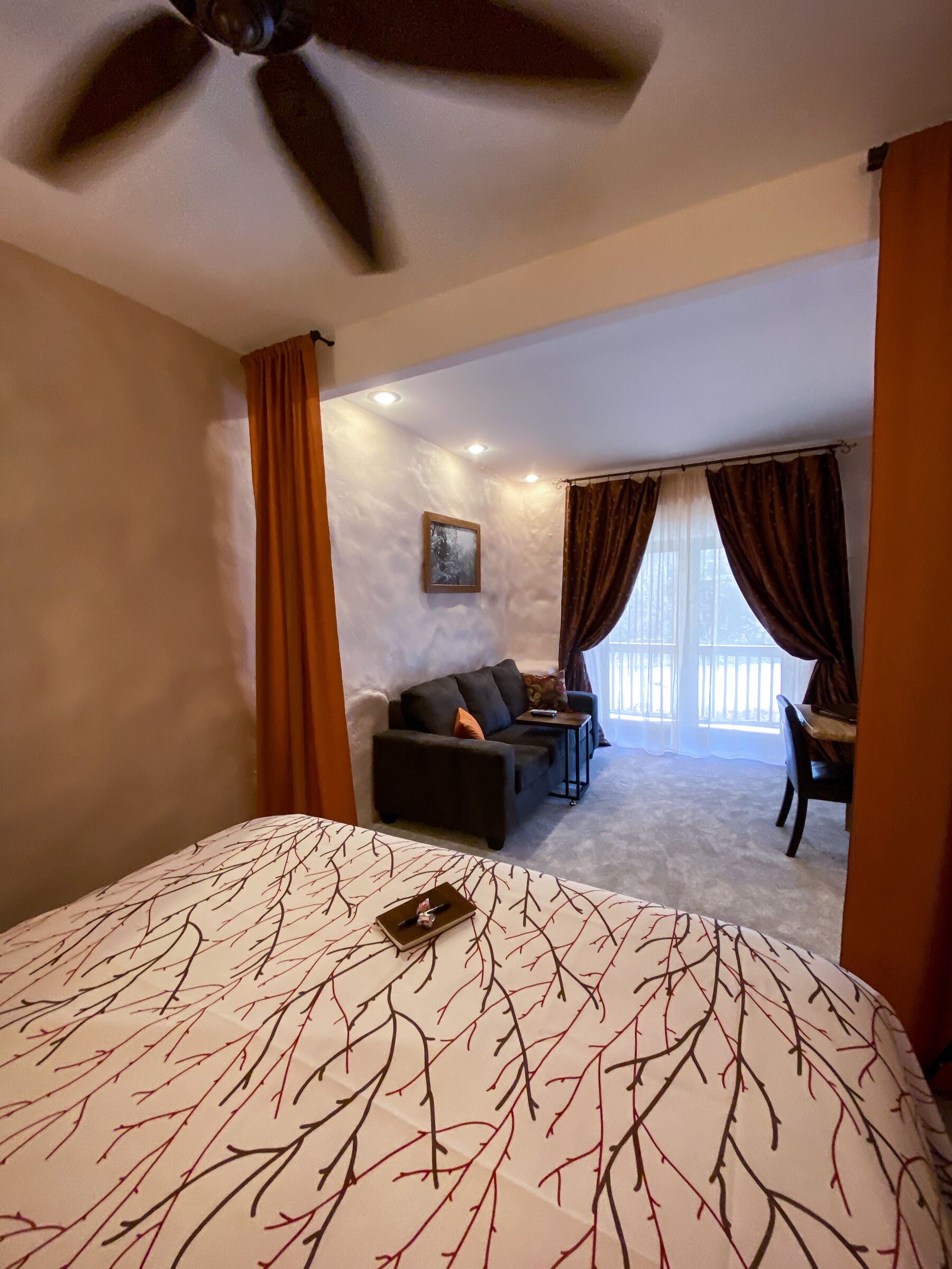 A bedroom with a large bed, a ceiling fan, a sofa, and a dining area with a table and chairs.