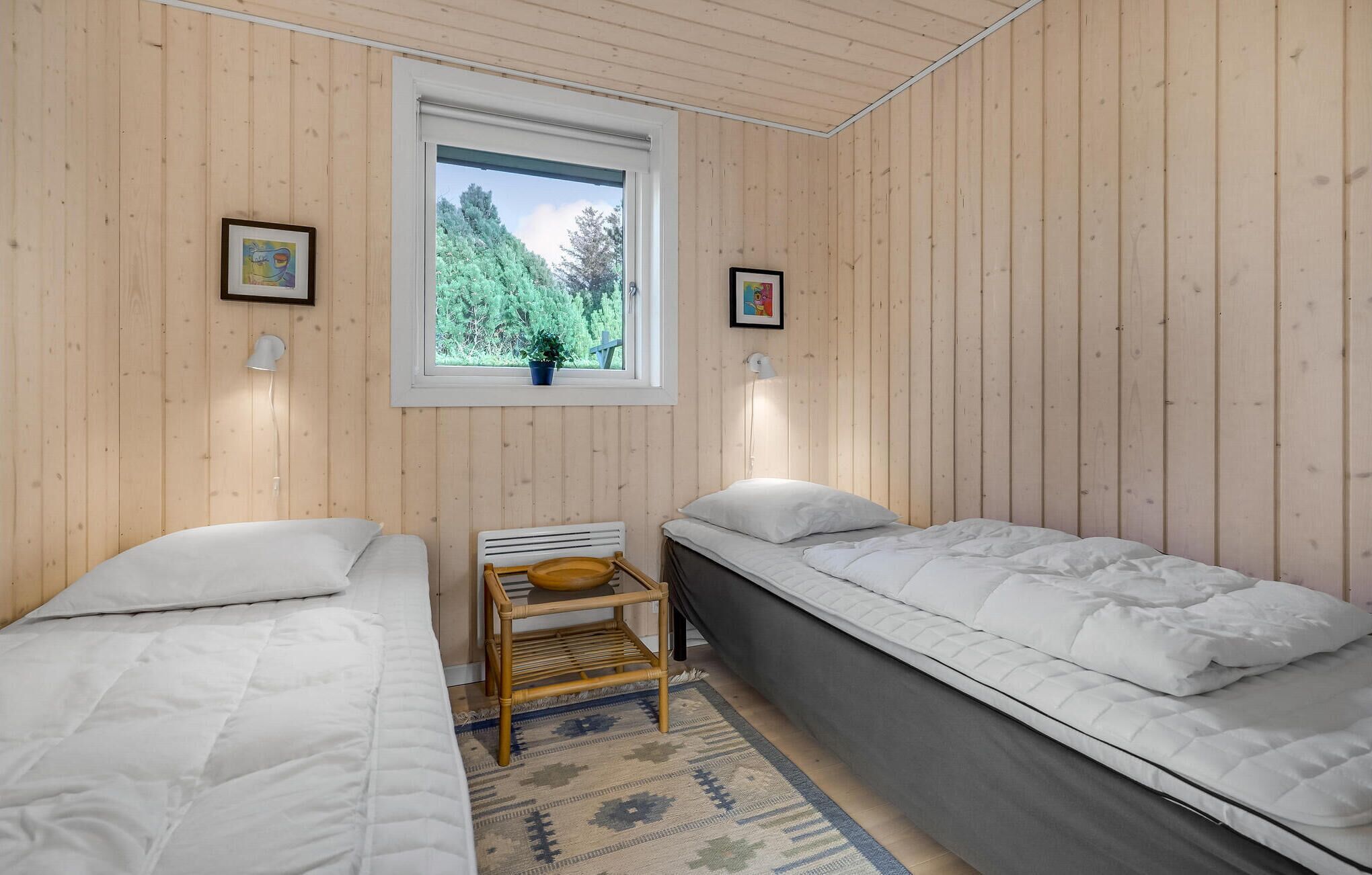 Una habitación con dos camas, una ventana que da a árboles y una mesita con un bol.