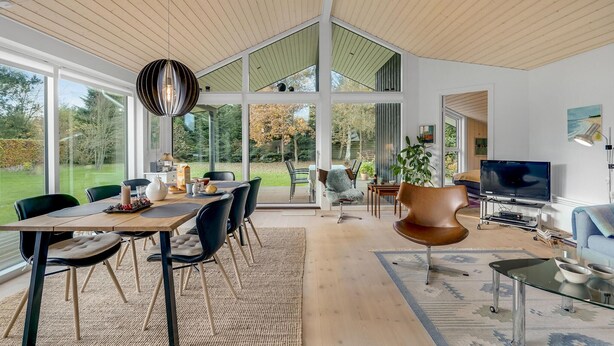 Un interior moderno con zona de comedor, sala de estar y un gran ventanal que da a un jardín.
