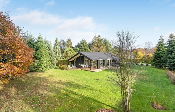 A modern house with a large deck, surrounded by a well-maintained lawn and dense trees. - Amazing home in Væggerløse with WiFi (Væggerløse)