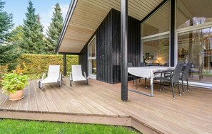 A modern outdoor patio with a wooden deck, white lounge chairs, and a dining table with chairs. - Amazing home in Væggerløse with WiFi (Væggerløse)