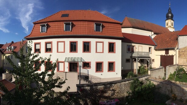 Un bâtiment européen traditionnel, avec un toit recouvert de tuiles rouges, une petite tour et un jardin agrémenté d’une balan çoire.