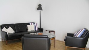 Un salon moderne avec un canapé en cuir noir, une table basse en verre et deux fauteuils noirs.