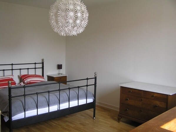 Un dormitorio con estructura metálica para la cama, una mesita de noche, un aparador y una lámpara colgante decorativa.