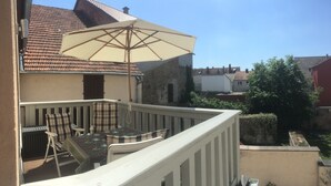 Un balcon avec une table et des chaises, un grand parasol et une vue sur les maisons voisines.
