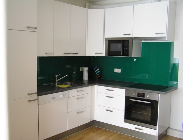 Una cocina moderna con gabinetes blancos, una encimera negra, un salpicadero verde, un microondas y un horno.