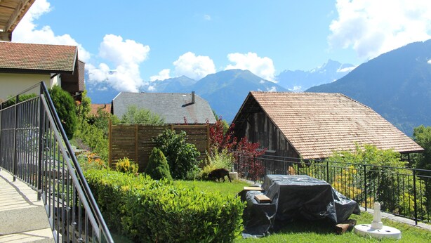 Ein Landhaus mit Garten, einem Holzzaun und Bergen im Hintergrund.